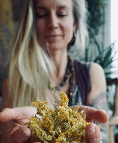 Karoline Karttunen för Karolines way of life håller gullris i händerna och tittar ner på örterna och blommorna